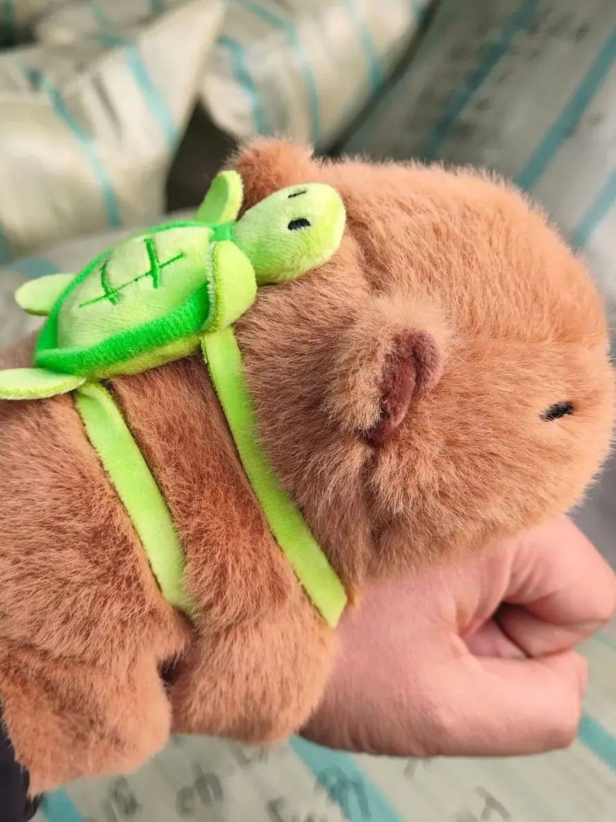 Bracelet peluche capybara portant une tortue verte sur le dos, tenu dans une main