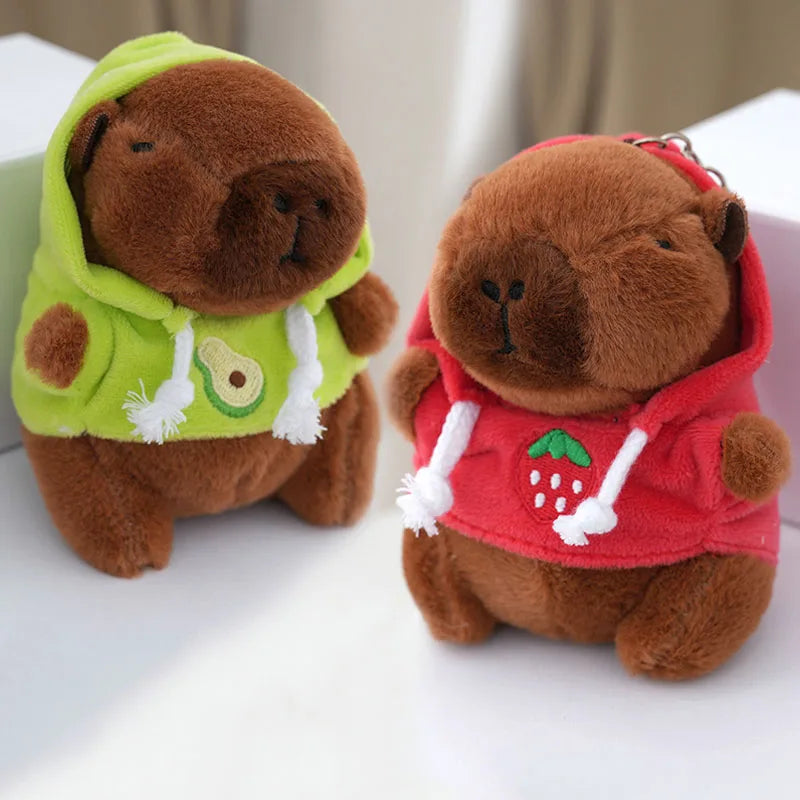 Deux porte-clés capybara en capuches verte à avocat et rouge à fraise, posés sur une table blanche
