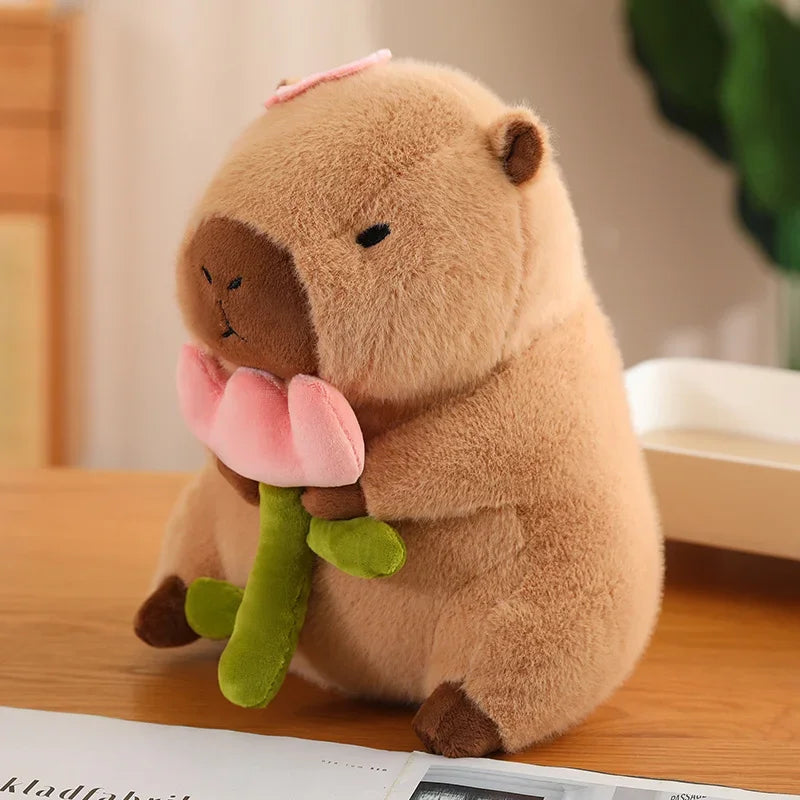 Peluche capybara beige tenant une fleur de lotus rose, assise sur une table en bois